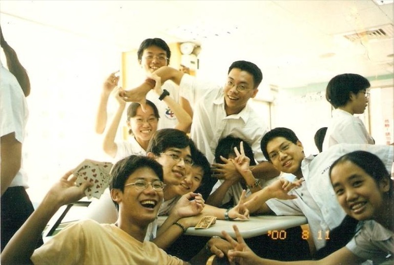 2000年8月一群年輕學生在室內桌前歡樂合影，有人手中拿著撲克牌。