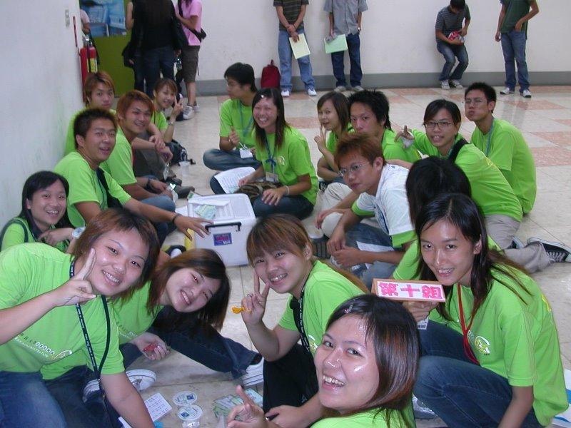 十多名穿著綠色統一營隊T恤的年輕男女在室內大廳席地而坐合影